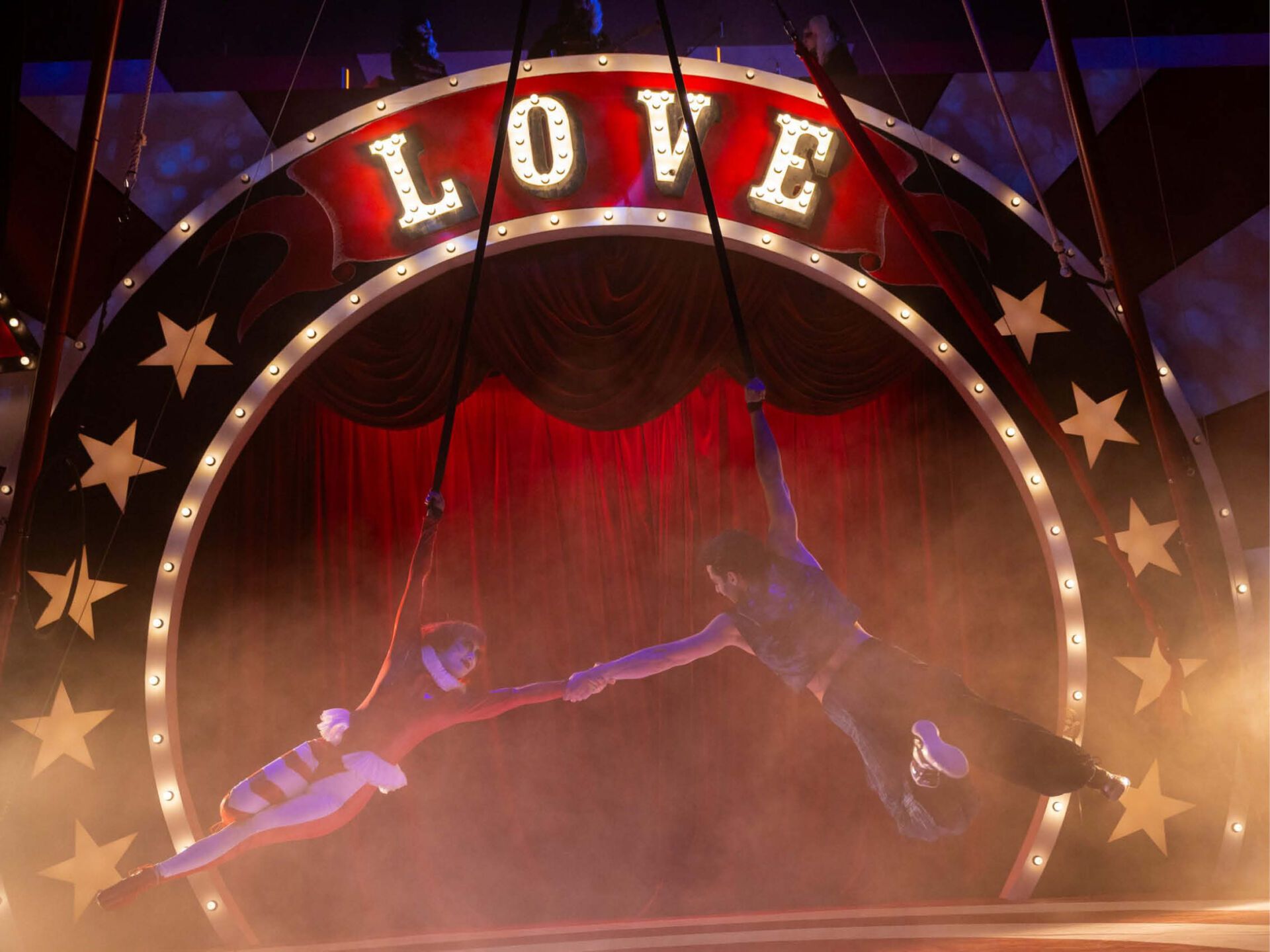In einer Zirkusarena sieht man zwei Akrobaten, ein Mann und eine Frau. Am Entre des Zirkus steht in großen Lettern: "LOVE".