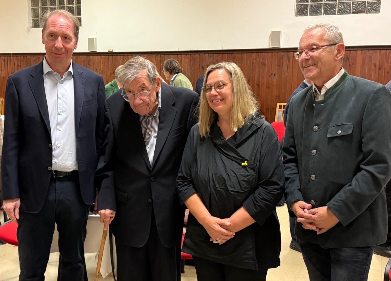 Vier stehende Personen. Sie lächeln und blicken seitlich an der kamera vorbei.