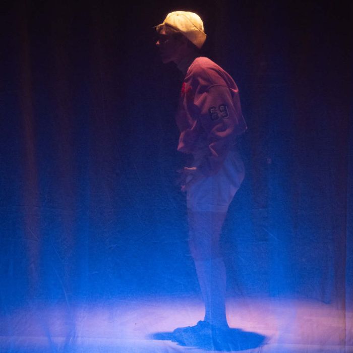 Hinter einem semitransparenten Vorhang steht eine Figur, die eine gelbe Kappe trägt und nach links ausgerichtet ist.